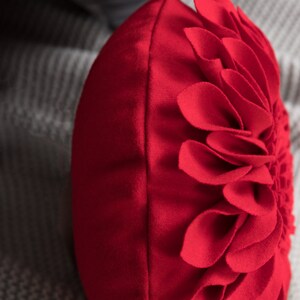 May include: Red round throw pillow with a large flower design made of fabric petals.