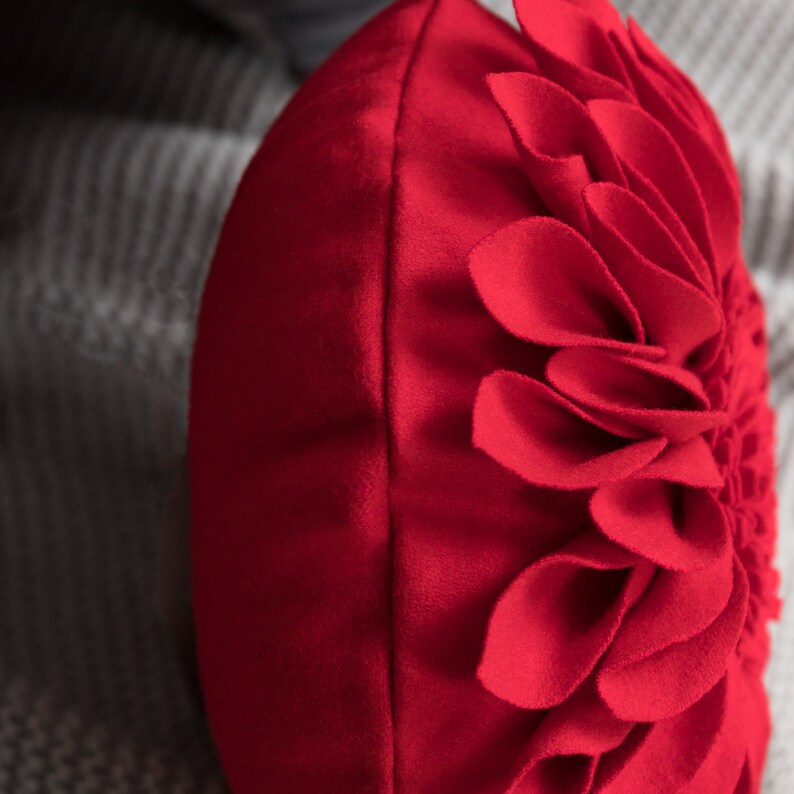 May include: Red round throw pillow with a large flower design made of fabric petals.