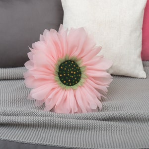May include: A large pink fabric flower with a green centre and yellow accents. The flower is sitting on a grey knitted blanket.