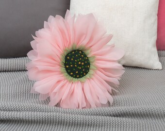 May include: A large pink fabric flower with a green center and yellow accents. The flower is sitting on a gray knitted blanket.