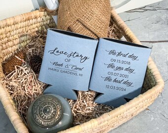 Op de afbeelding: Twee blauwe blikjeskoelers met witte tekst. Eén koeler zegt "Love Story of Noah & Carol, Haiku Gardens, HI". De andere koeler zegt "The first day 09.15.2018, The yes day 03.07.2021, The best day 12.03.2024".