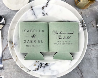 Peut inclure: Deux refroidisseurs de canettes verts avec du texte noir. Un refroidisseur dit "Isabella & Gabriel Nov 12, 2024". L'autre refroidisseur dit "To have and to hold and to keep your beer cold!"