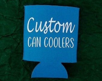 May include: A blue can cooler with the words "Custom CAN COOLERS" in white script. The cooler has a rectangular top with a curved bottom. The background is a dark green, textured fabric. The logo "BESPOKE CAN COOLERS" is in the bottom left corner.