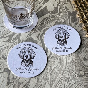 Op de afbeelding: Twee ronde witte onderzetters met zwarte tekst en een zwart-witte illustratie van een hond. De tekst op de onderzetters luidt "Wendy Do Too!" en "Alexa & Branden 19.12.2024".
