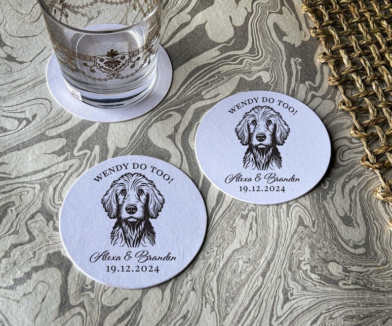 Op de afbeelding: Twee ronde witte onderzetters met zwarte tekst en een zwart-witte illustratie van een hond. De tekst op de onderzetters luidt "Wendy Do Too!" en "Alexa & Branden 19.12.2024".
