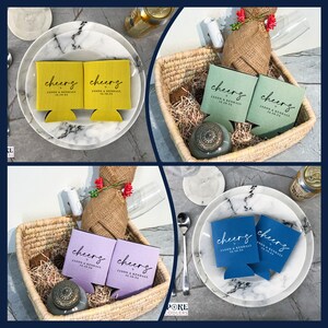 Pu&ograve; includere: Un assortimento di portabevande per lattine in giallo, verde, viola e blu. Ogni portabevande presenta la scritta "cheers" in corsivo, insieme a un nome e una data. I portabevande sono disposti su piatti e in un cestino intrecciato.