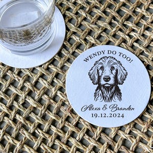 Op de afbeelding: Ronde witte onderzetter met zwarte tekst en een zwart-witte illustratie van een hond. De tekst luidt "Wendy Do Too! Alexa & Branden 19.12.2024".