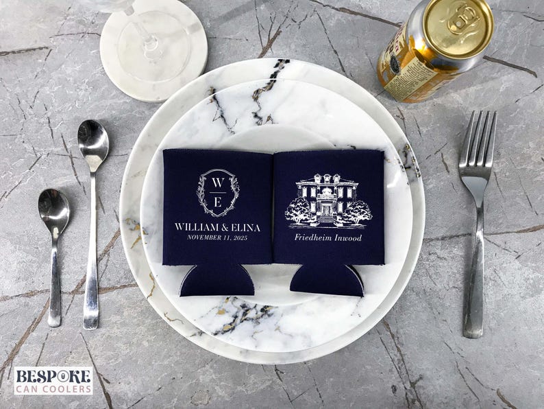 May include: Two navy blue can coolers with white text and designs. One cooler features a monogram with the initials "W" and "E" and the text "William & Elina, November 11, 2023". The other cooler features a black and white illustration of a house with the text "Friedheim Innwood".
