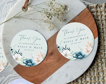 May include: Two round thank you cards with a watercolor floral design in shades of blue, green, white, and pink. The text on the cards reads "Thank You for celebrating with us Stacy & Mark 22.04.24".