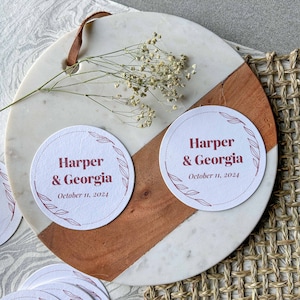 May include: Set of six white paper coasters with a red floral design and the text "Harper & Georgia" and the date "October 11, 2024".