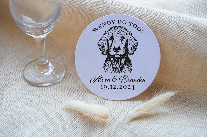 Op de afbeelding: Ronde witte onderzetter met zwarte tekst die "Wendy Do Too!" luidt en een zwart-witte illustratie van een hond. De tekst onder de hond luidt "Alexa & Branden 19.12.2024".