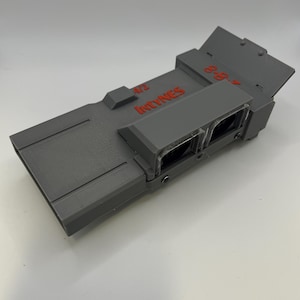 May include: A gray, rectangular device with the text "472 Intynes" in red. The device has two clear, rectangular openings and a hinged top. The device is made of a matte material.