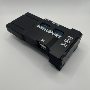 Op de afbeelding: Een zwart elektronisch apparaat met de tekst "IntelliPort" en "7-88" erop gedrukt. Het heeft meerdere poorten, waaronder USB- en DB9-connectoren. Het apparaat heeft ook de tekst "THIS LINE" erop gedrukt.