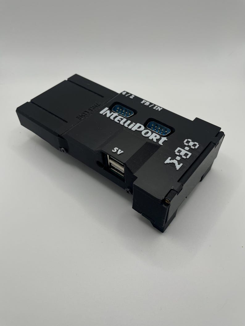 Op de afbeelding: Een zwart elektronisch apparaat met de tekst "IntelliPort" en "7-88" erop gedrukt. Het heeft meerdere poorten, waaronder USB- en DB9-connectoren. Het apparaat heeft ook de tekst "THIS LINE" erop gedrukt.