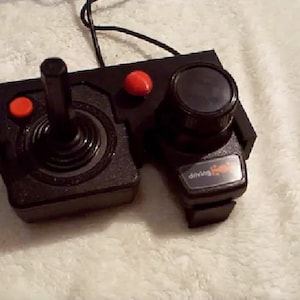 May include: A black Atari 2600 joystick with a red button and a black knob. The joystick has the text "driving" and a small car icon on it.