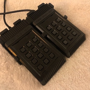 May include: Two black handheld controllers with a grid of buttons and the text "MICRO-COMPUTER" on the top. The controllers are connected by a black cable.