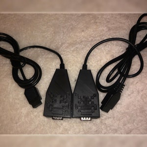 May include: Two black video game controller adapters with a space invader graphic. The adapters are connected to black cables.