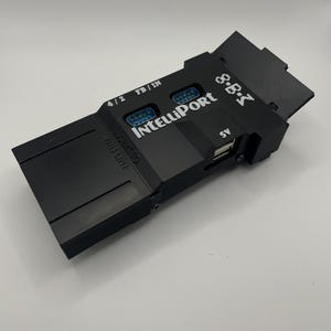 May include: A black electronic device with the text "IntelliPort" and "S.B.I" printed on it. It has multiple ports, including a USB port and two DB9 connectors. The device also has the text "4/2" and "FB/IN" printed on it.