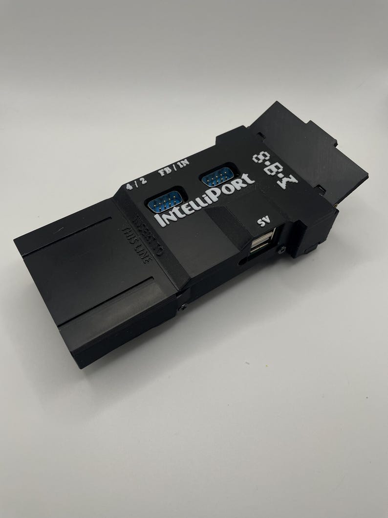 Op de afbeelding: Een zwart elektronisch apparaat met de tekst "IntelliPort" en "S.B.I" erop gedrukt. Het heeft meerdere poorten, waaronder een USB-poort en twee DB9-connectoren. Het apparaat heeft ook de tekst "4/2" en "FB/IN" erop gedrukt.