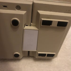 May include: A beige electronic device with a white label on the side. The device has four black rubber feet on the bottom.