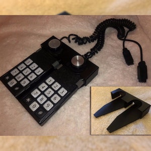 May include: A black vintage telephone with two number pads and two rotary dials. The phone has a coiled cord and a black connector.