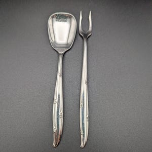 May include: A set of two silver-plated serving utensils with an ornate floral design. The set includes a spoon and a fork.