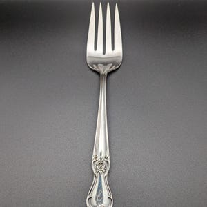 May include: A silver fork with an ornate handle and a floral design. The fork has a monogrammed letter "S" on the handle.