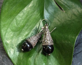 May include: A pair of silver earrings with black gemstone drops. The earrings feature intricate filigree designs and are suspended from silver hooks.