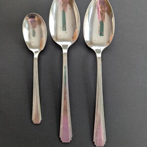May include: Three silver spoons of different sizes. The spoons have a decorative design on the handle and a rounded bowl.