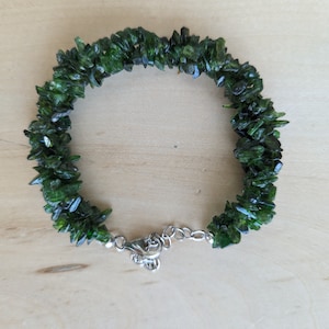 May include: A green gemstone bracelet made of small, irregular chips of green aventurine. The bracelet has a silver clasp.