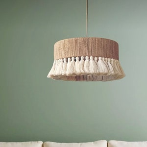 May include: A round, woven, beige lampshade with a white fringe hangs from the ceiling above a white sofa and a black and white patterned coffee table.