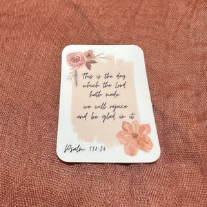 May include: A white card with a floral design and the text "This is the day which the Lord hath made we will rejoice and be glad in it. Psalm 111:24".