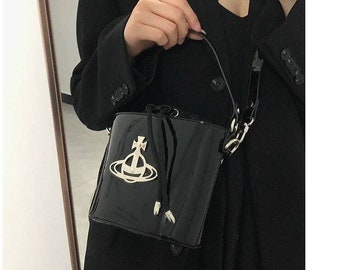 May include: A black patent leather bucket bag with a silver orb and cross charm. The bag has a top handle and a detachable shoulder strap.