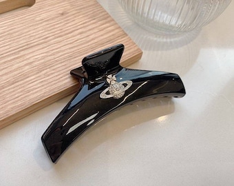 May include: Black plastic hair claw with a silver orb charm featuring a circle with a smaller circle inside and rhinestones.