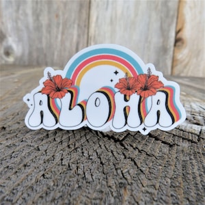 May include: A white sticker with the word "ALOHA" in a retro font with rainbow stripes behind the letters. Two red hibiscus flowers are above the word.