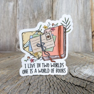 May include: A sticker with a pink book, envelopes, and flowers. The text reads "I live in two worlds one is a world of books."