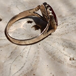 May include: A gold ring with a red gemstone set in a detailed, ornate setting. The ring is on a white background.
