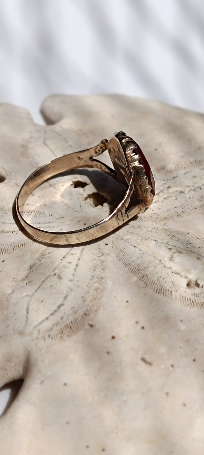 May include: A gold ring with a red gemstone set in a detailed, ornate setting. The ring is on a white background.