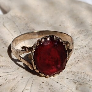 May include: A silver ring with a large, oval-shaped, dark red gemstone set in a decorative, gold-toned bezel.
