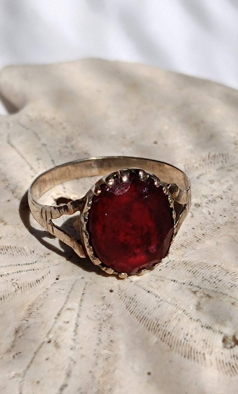 May include: A silver ring with a large, oval-shaped, dark red gemstone set in a decorative, gold-toned bezel.