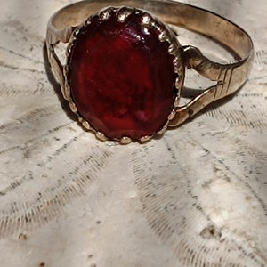 May include: A gold ring with a red gemstone set in a decorative bezel. The ring has a simple band with a twisted design.