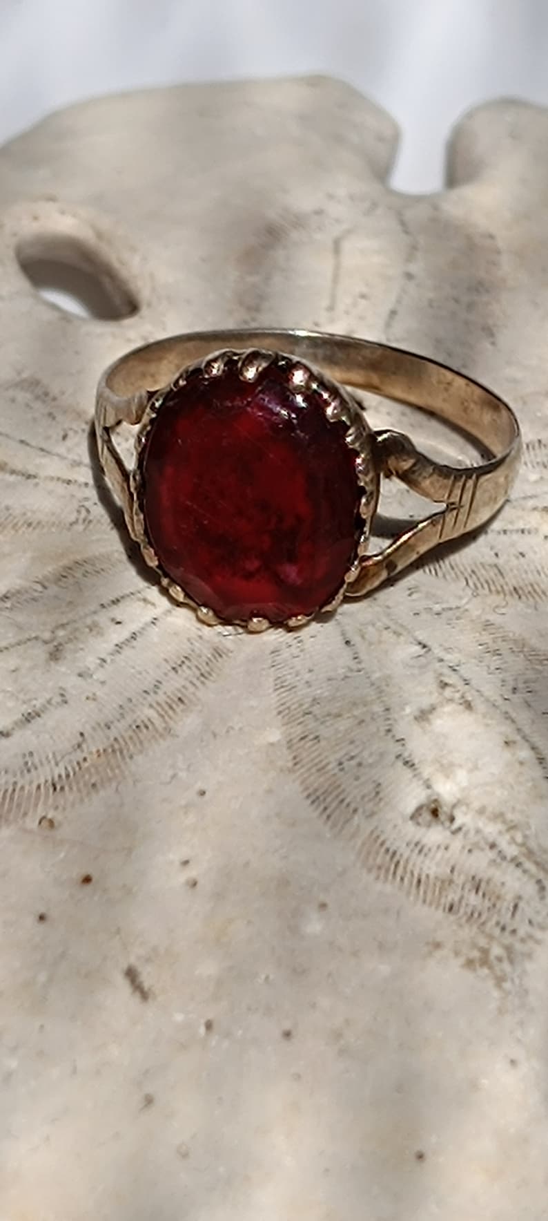 May include: A gold ring with a red gemstone set in a decorative bezel. The ring has a simple band with a twisted design.