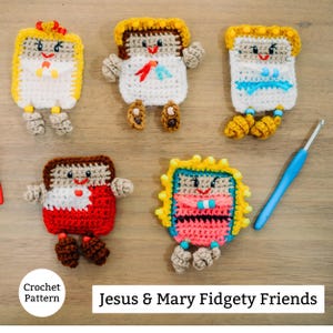 May include: A selection of brightly coloured, crocheted figures, each with distinct designs and features. The figures are square-shaped with arms, legs, and smiling faces. The text "Jesus & Mary Fidgety Friends" is displayed below the figures. A blue crochet hook is also visible.