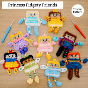 May include: A collection of colorful, handmade crochet dolls, each with unique features and outfits. The dolls are arranged on a wooden surface, with the text "Princess Fidgety Friends" at the top. A crochet hook is visible in the background. The dolls are approximately 4 inches tall.
