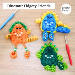 Puede incluir: Juguetes fidget de dinosaurios de ganchillo en naranja, azul y verde. Cada dinosaurio tiene un diseño único, con detalles como púas y acentos de diferentes colores. La imagen incluye el texto "Dinosaur Fidgety Friends" y "Crochet Pattern".