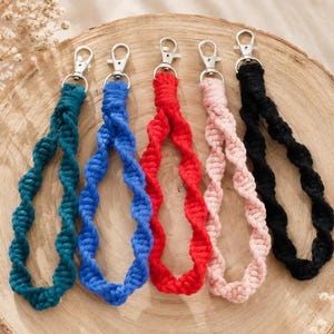 Pode incluir: Cinco porta-chaves de pulso em macramé com um design de corda torcida nas cores azul-petróleo, azul-real, vermelho, rosa claro e preto. Cada porta-chaves está preso a um mosquetão de metal prateado para prender chaves ou acessórios.