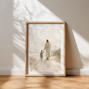 May include: A framed print showing a figure in a white robe holding hands with a child, walking through a cloudy landscape. The artwork has a soft colour palette and is presented in a wooden frame.