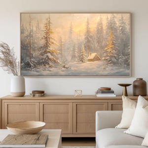 May include: A painting of a snowy forest scene with a small cabin in the distance. The trees are covered in snow and the sun is shining through the branches. The painting is framed in a light wood frame.