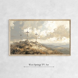 May include: A painting of three wooden crosses on a hilltop with a cloudy sky in the background. The crosses are silhouetted against the sky, and the hill is covered in brown grass. The painting is framed in a light wood frame.