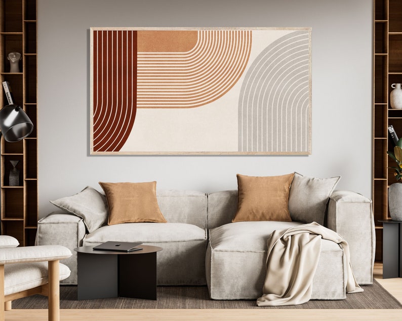 May include: Abstract art print with a geometric design featuring curved lines in shades of brown, orange, and gray. The print is framed and hanging on a wall above a white sofa.